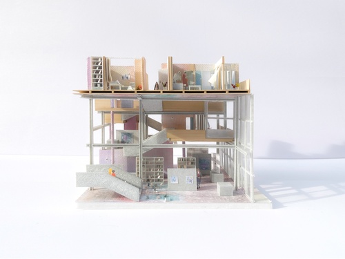 Section Model of a residence with pink and white walls with multiple grey staircases. A reading area is on the ground level and a bath and bedroom are located above.