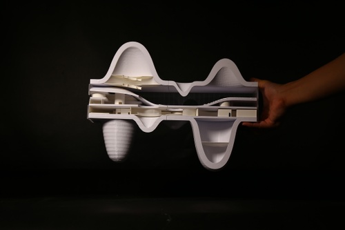 Curved sectional model with interior views held by student's hand on a black backdrop. 