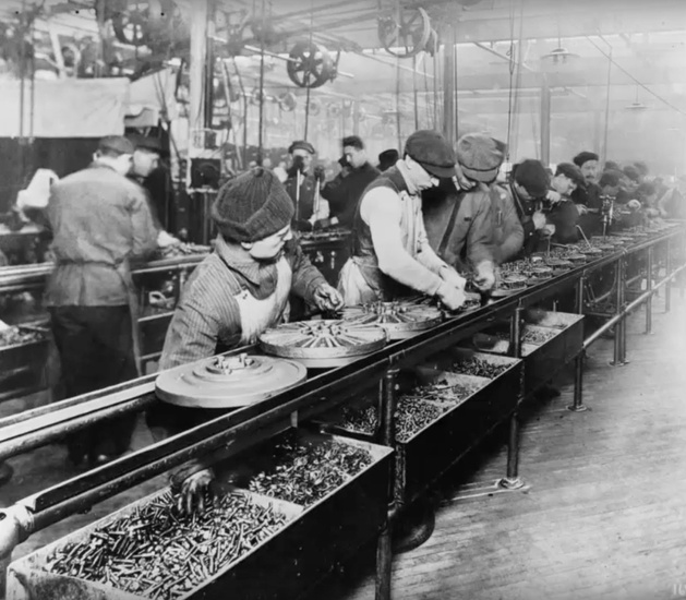 Workers on the first moving assembly line, at the Ford Highland Park Plant, put V-shaped magnets on Model T flywheels to make one-half of the flywheel magneto, 1913.