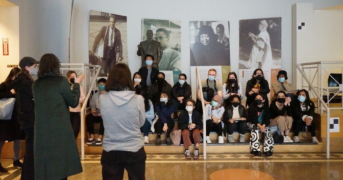 Students sit on a staircase while faculty (standing) speak to them